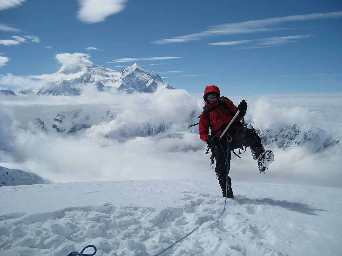 A climber heading up a snowy summit above the clouds