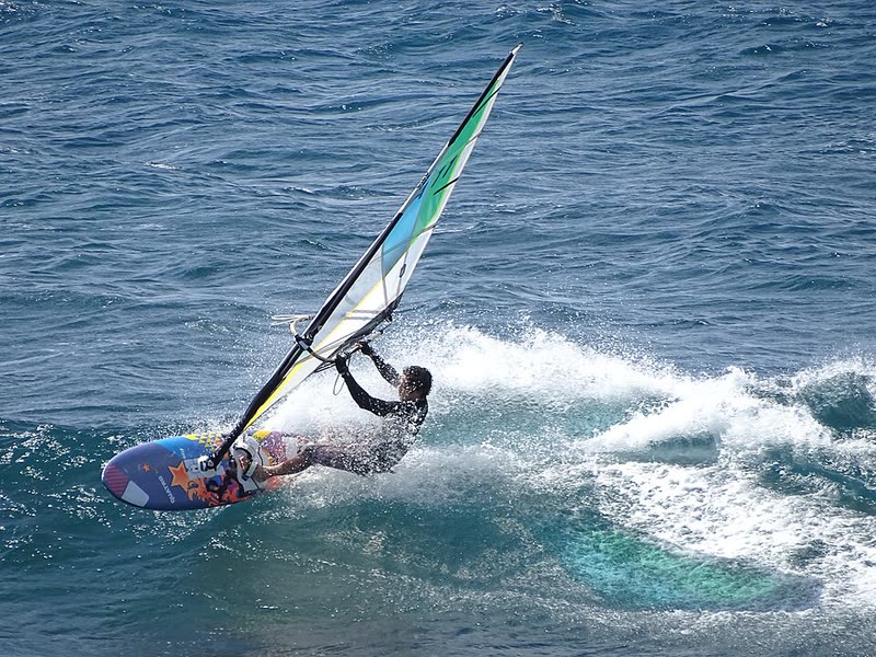 A windsurfer carves across a breaking wave at Hoʻokipa on Maui's north shore.