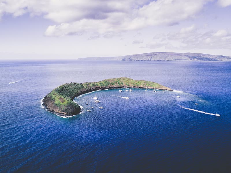 Aerial view of the crescent-shaped Molokini crater, with boats moored in its sheltered snorkeling waters.