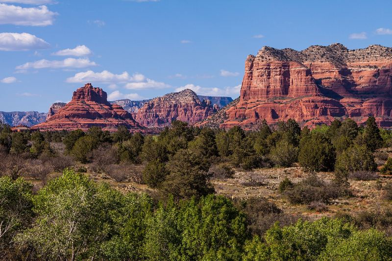 Bell Rock and Courthouse Butte rising above green juniper and pinyon scrub under a blue sky.