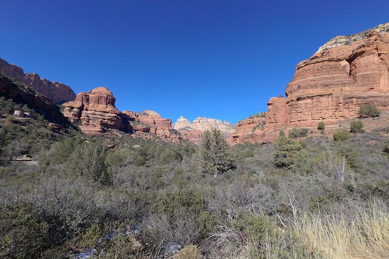 Red rock buttes and cliffs lining Boynton Canyon above green desert scrub under a clear blue sky.