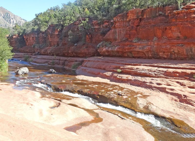 Oak Creek rushing down the slick red sandstone chute at Slide Rock State Park beneath red rock canyon walls.